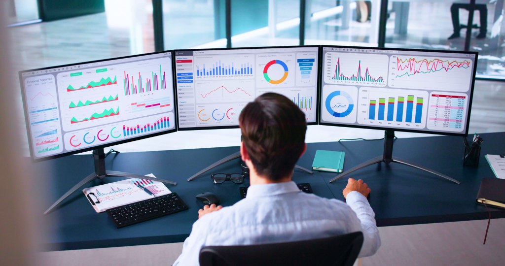 A data leader at a multi-monitor analytics workstation, seen from behind